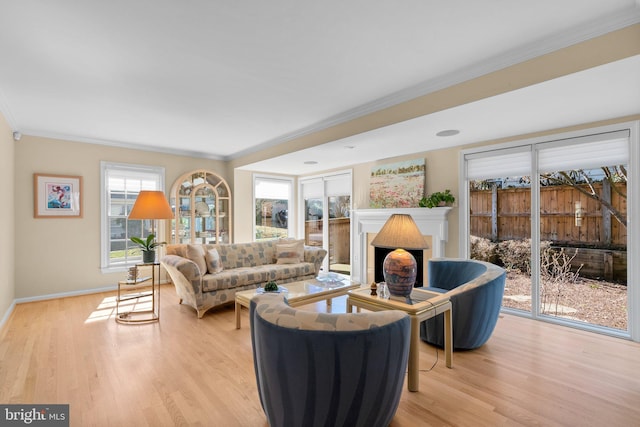 living area featuring a brick fireplace, light wood-type flooring, baseboards, and ornamental molding