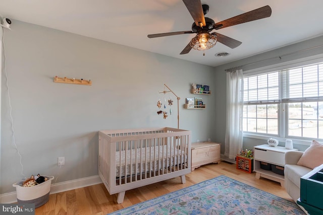 bedroom with baseboards, visible vents, a ceiling fan, wood finished floors, and a nursery area