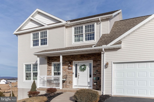 multi unit property with covered porch, stone siding, a shingled roof, and an attached garage