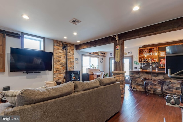 living room featuring bar, visible vents, beamed ceiling, dark wood finished floors, and a wood stove