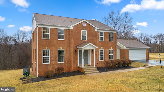 colonial home featuring a garage, driveway, brick siding, and a front yard