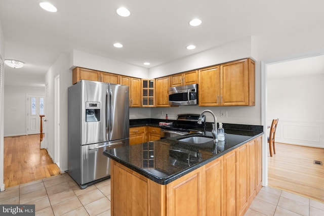 kitchen featuring light tile patterned floors, appliances with stainless steel finishes, a sink, dark stone counters, and a peninsula