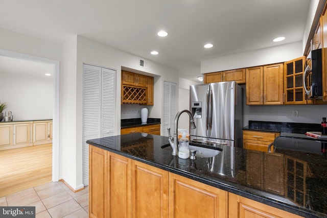 kitchen with stainless steel appliances, glass insert cabinets, a sink, dark stone countertops, and a peninsula