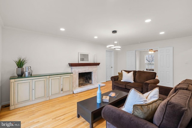 living area with ceiling fan, crown molding, light wood-style floors, a fireplace, and recessed lighting