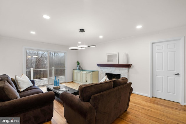 living room featuring crown molding, recessed lighting, a fireplace, and light wood-style flooring