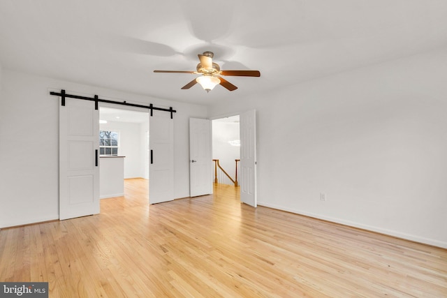 unfurnished room featuring light wood-type flooring, a barn door, baseboards, and a ceiling fan