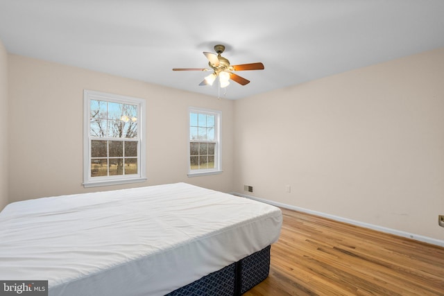 bedroom with ceiling fan, wood finished floors, visible vents, and baseboards