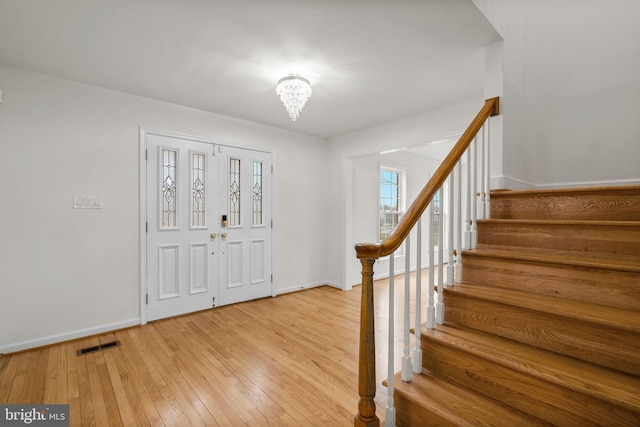 entrance foyer featuring baseboards, visible vents, an inviting chandelier, stairs, and light wood-style floors