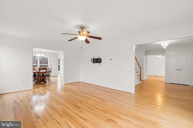 unfurnished living room with light wood-style flooring, stairway, baseboards, and ceiling fan with notable chandelier