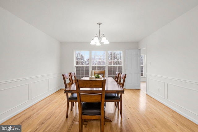 dining area with a chandelier, light wood finished floors, wainscoting, and a decorative wall