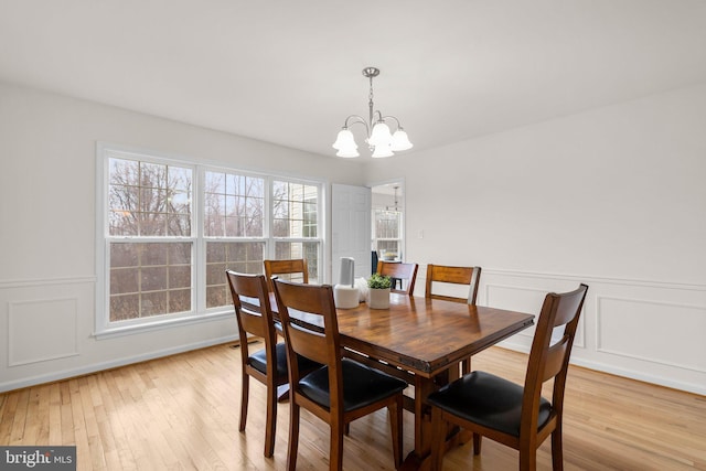 dining room featuring light wood-style floors, wainscoting, a notable chandelier, and a decorative wall