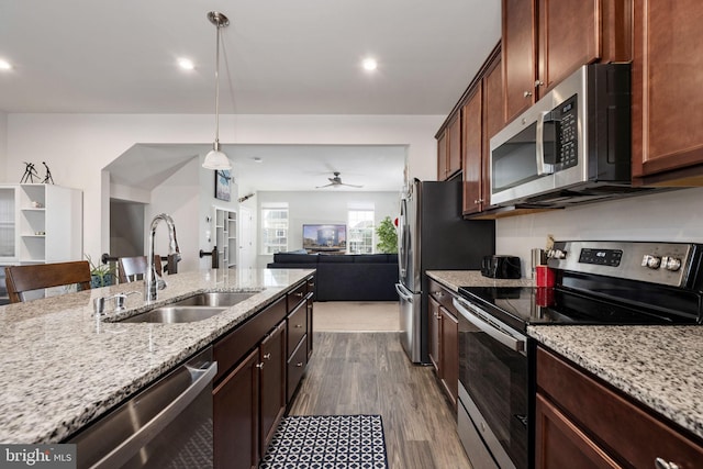 kitchen with stainless steel appliances, a sink, open floor plan, light stone countertops, and dark wood finished floors