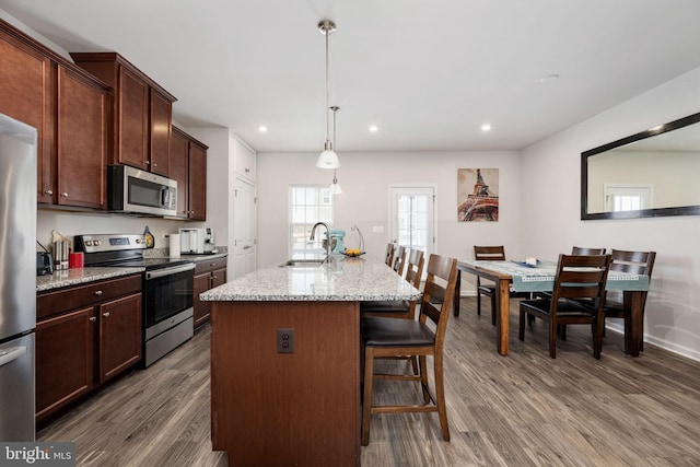 kitchen featuring dark wood finished floors, an island with sink, appliances with stainless steel finishes, a kitchen breakfast bar, and a sink