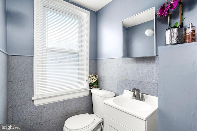 half bathroom featuring toilet, vanity, and tile walls