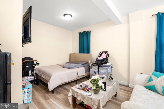 bedroom with light wood-style floors, baseboards, and beam ceiling