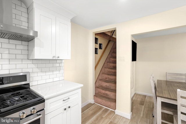 kitchen featuring wall chimney exhaust hood, light wood finished floors, stainless steel range with gas stovetop, and white cabinets