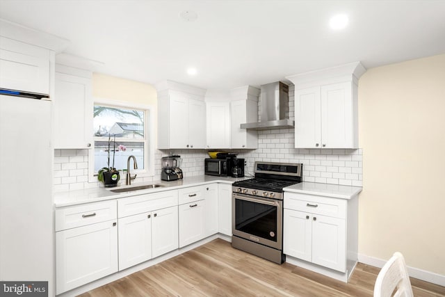 kitchen featuring stainless steel range with gas cooktop, light countertops, white cabinets, a sink, and wall chimney range hood