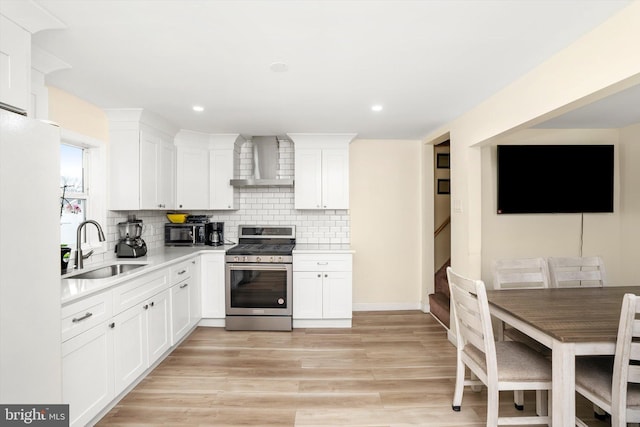 kitchen with light countertops, decorative backsplash, a sink, wall chimney range hood, and stainless steel gas range