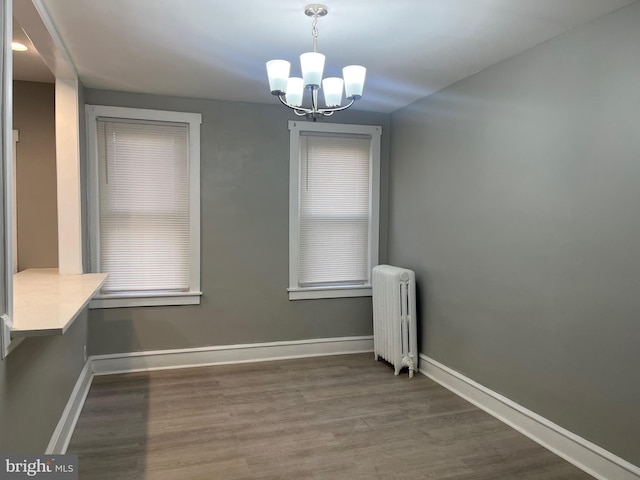 unfurnished dining area with wood finished floors, baseboards, radiator heating unit, and an inviting chandelier