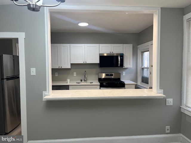 kitchen featuring appliances with stainless steel finishes, a peninsula, light countertops, white cabinetry, and a sink