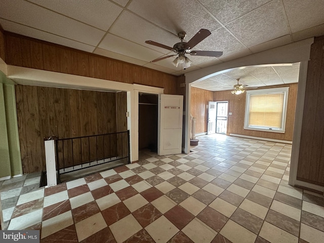 unfurnished room featuring a paneled ceiling, ceiling fan, and wooden walls