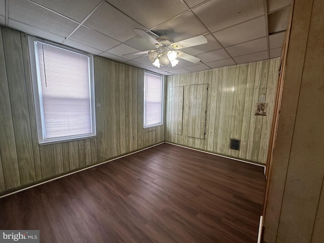 unfurnished room featuring a drop ceiling, dark wood finished floors, wooden walls, and ceiling fan