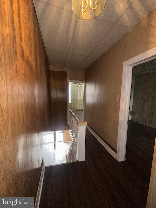 hall featuring wooden walls, baseboards, wood finished floors, and an upstairs landing