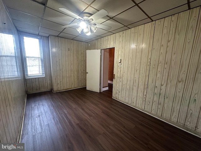 unfurnished room featuring a paneled ceiling, wooden walls, a ceiling fan, and dark wood-type flooring