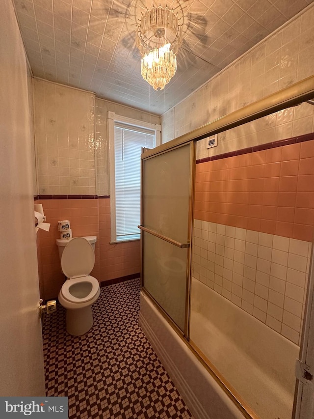 bathroom featuring tile walls, toilet, combined bath / shower with glass door, a chandelier, and tile patterned floors