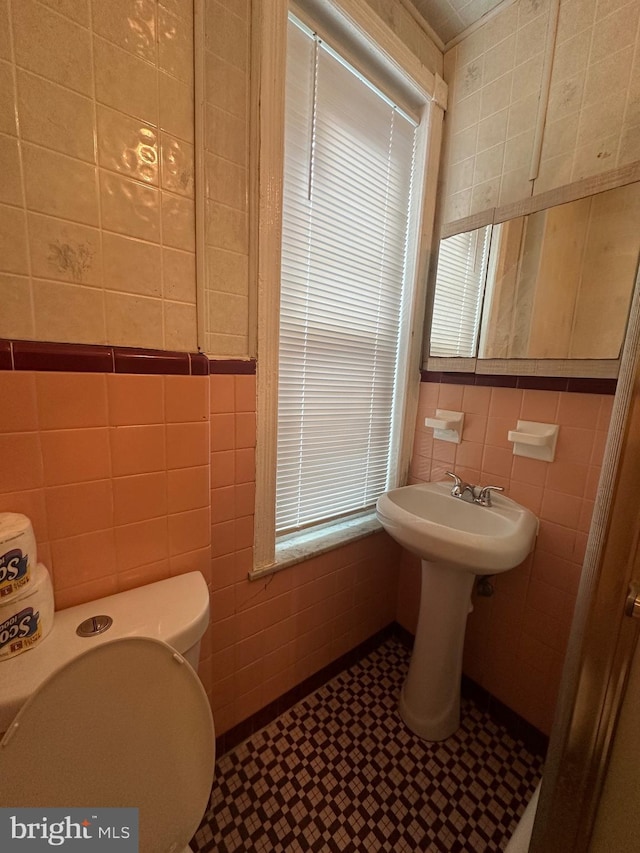 half bath featuring toilet, a sink, and tile walls