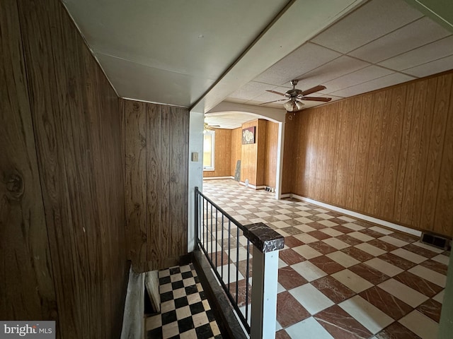 hall with arched walkways, wooden walls, visible vents, and tile patterned floors