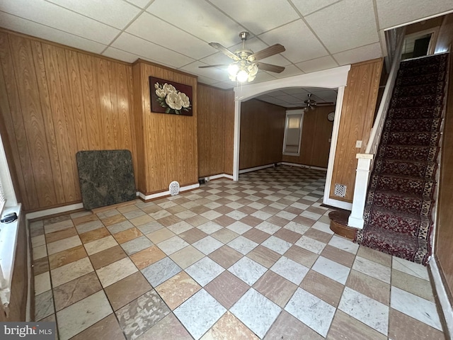 empty room with arched walkways, ceiling fan, wood walls, and stairway