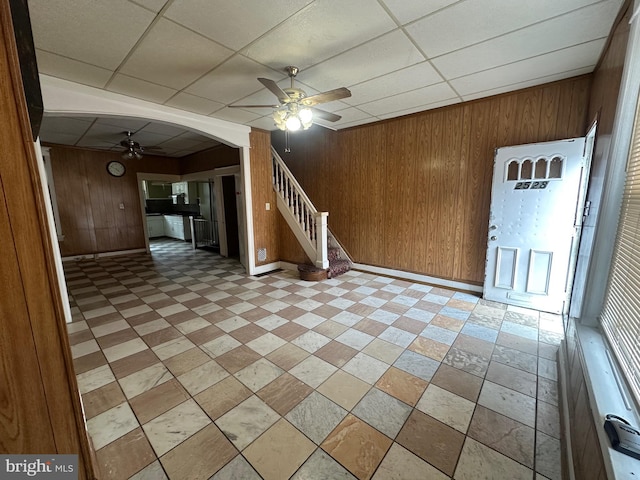 interior space with wooden walls, arched walkways, a drop ceiling, ceiling fan, and stairway