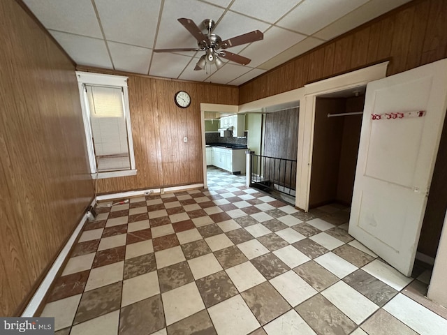 interior space with wooden walls, baseboards, a drop ceiling, and tile patterned floors