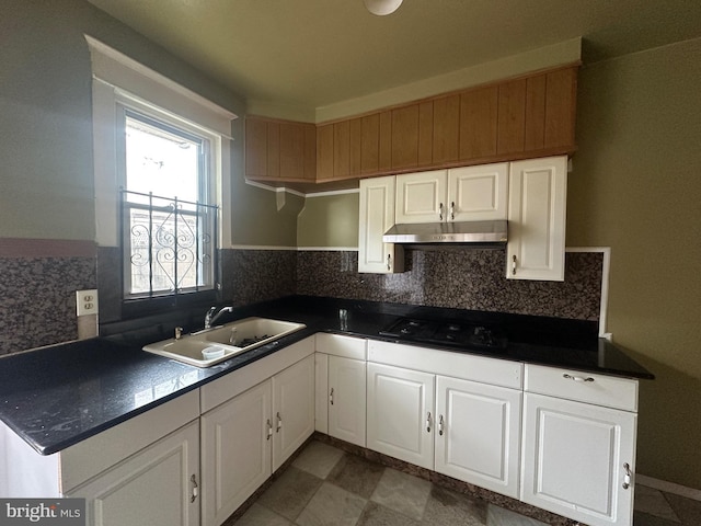 kitchen featuring dark countertops, a sink, white cabinetry, and under cabinet range hood