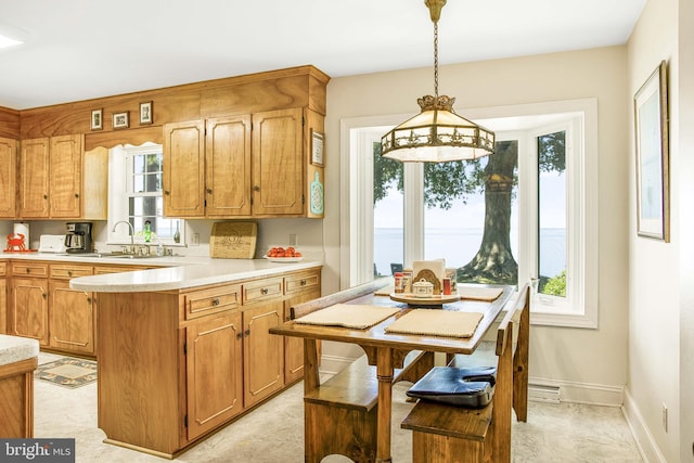 kitchen featuring baseboards, decorative light fixtures, a peninsula, light countertops, and a sink