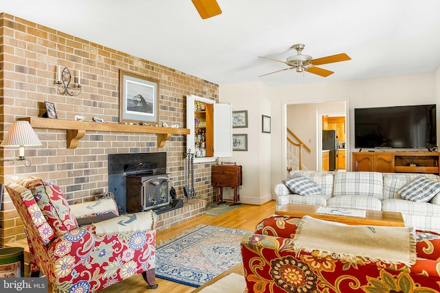 living area featuring a wood stove, ceiling fan, baseboards, and wood finished floors