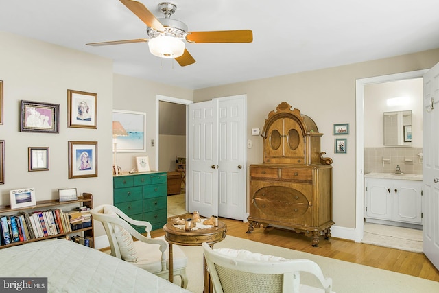 bedroom featuring ceiling fan, connected bathroom, a sink, baseboards, and light wood-type flooring