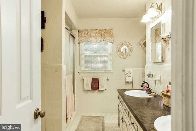 bathroom featuring double vanity, a shower stall, tile walls, and a sink