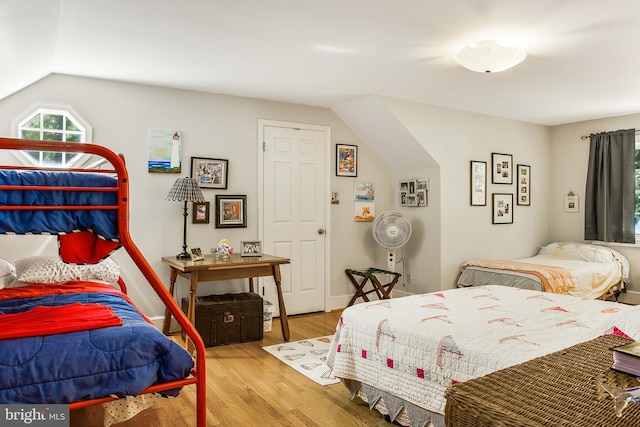 bedroom featuring multiple windows, baseboards, vaulted ceiling, and wood finished floors