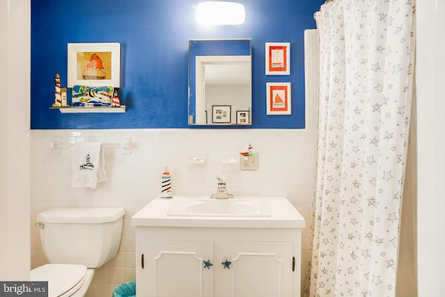 bathroom with wainscoting, vanity, toilet, and tile walls