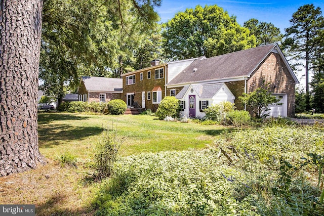 view of front of house with a garage, brick siding, a chimney, and a front yard