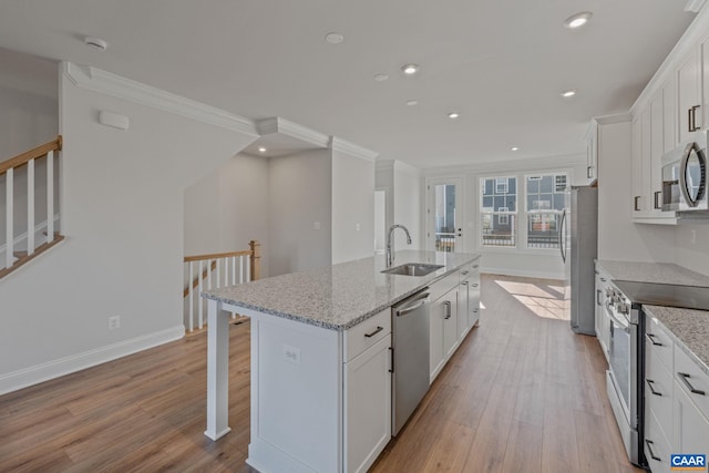 kitchen with light wood finished floors, a center island with sink, appliances with stainless steel finishes, white cabinetry, and a sink