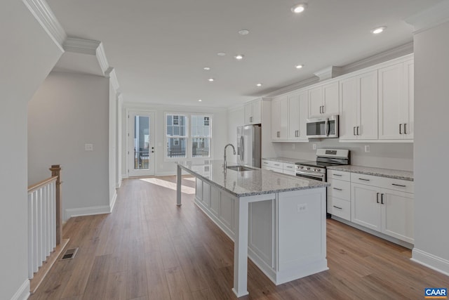 kitchen with crown molding, a center island with sink, stainless steel appliances, white cabinets, and wood finished floors