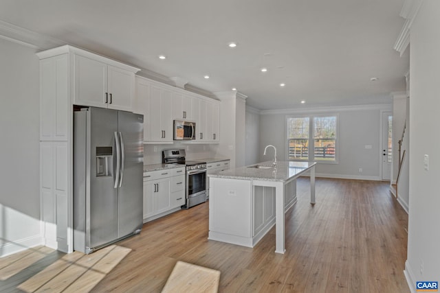 kitchen with a center island with sink, white cabinets, stainless steel appliances, crown molding, and a sink