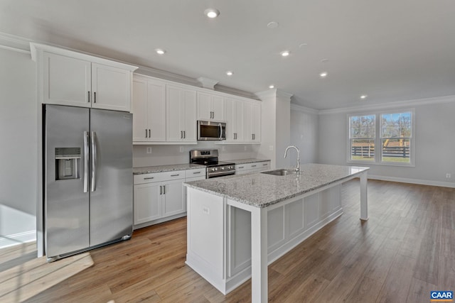 kitchen with a center island with sink, stainless steel appliances, ornamental molding, white cabinetry, and a sink