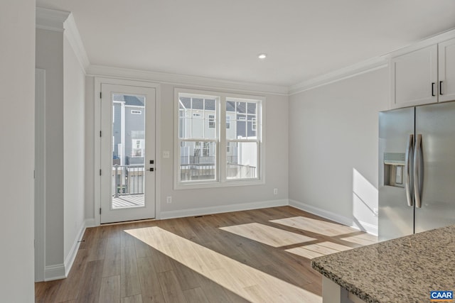 doorway with ornamental molding, light wood-style flooring, and baseboards