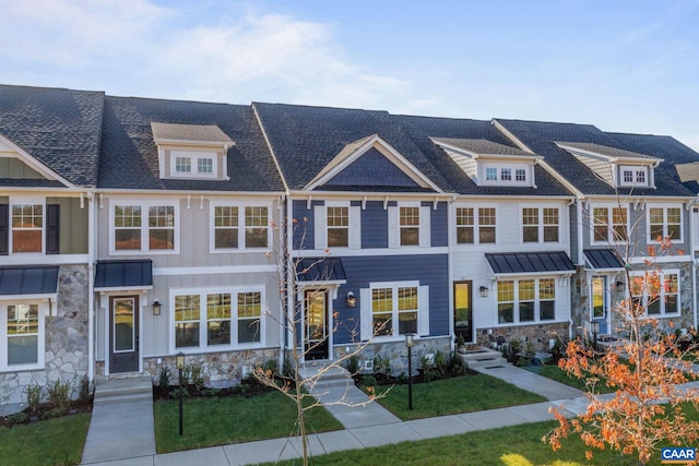 townhome / multi-family property with stone siding, a front lawn, roof with shingles, and board and batten siding