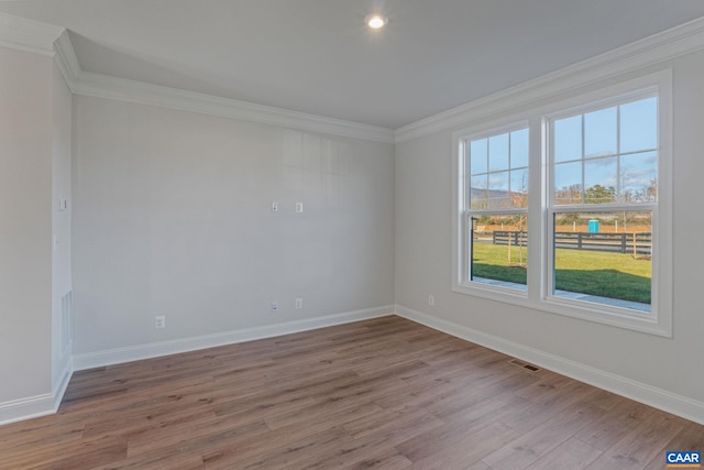 spare room with ornamental molding, visible vents, baseboards, and wood finished floors