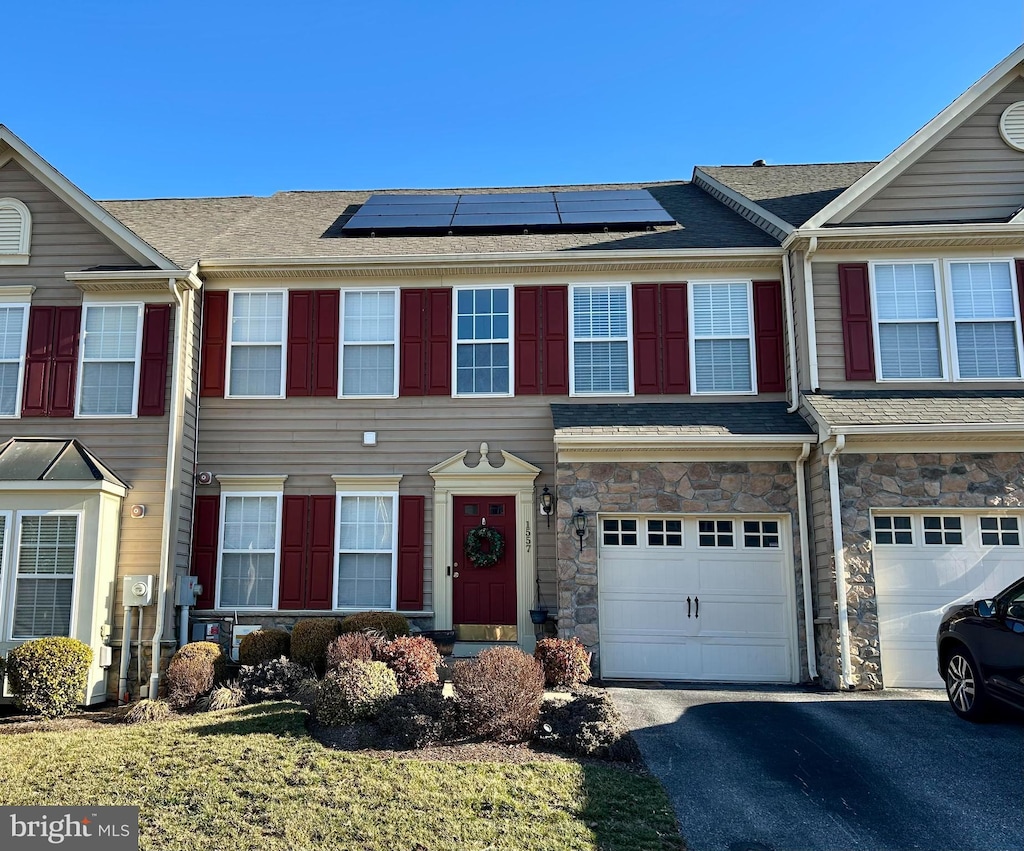 multi unit property featuring a garage, driveway, stone siding, and solar panels